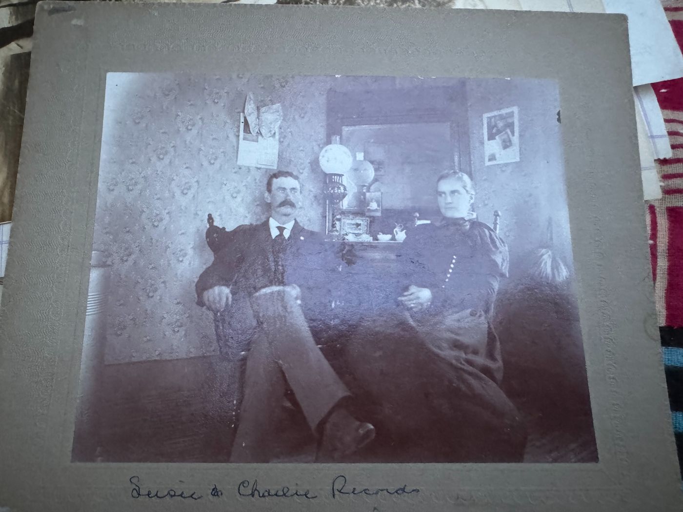 A seated couple posed in a wallpapered parlor in a late-1800s cabinet photograph.
